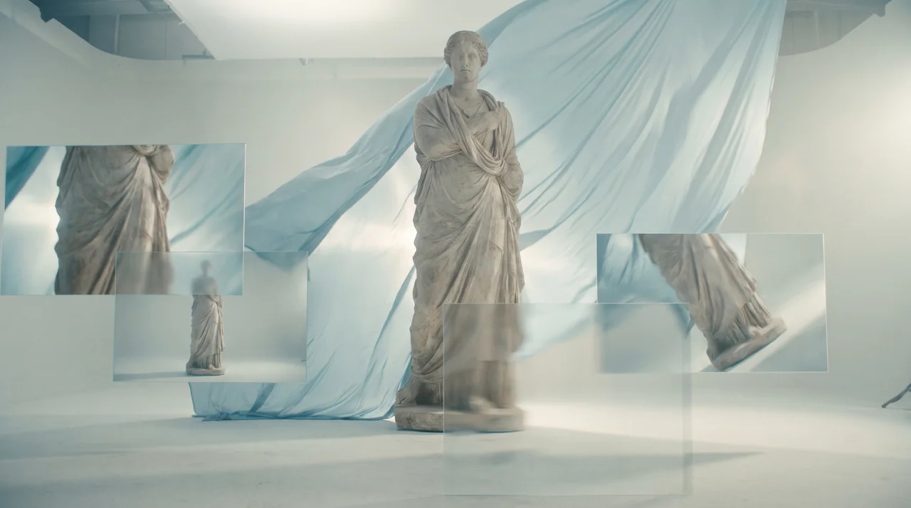 Statue in einem hellen Studio mit schwebenden Glasrahmen und blauem Tuch